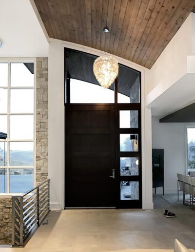 Modern entryway with a large wooden door and an ornate chandelier, featuring stone accents and a vaulted wooden ceiling.