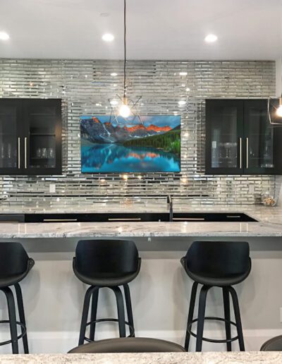 Modern kitchen interior with a breakfast bar, black stools, and a colorful artwork above the countertop.