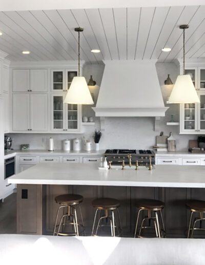 A modern kitchen with white cabinetry, stainless steel appliances, a central island with bar stools, and pendant lights.