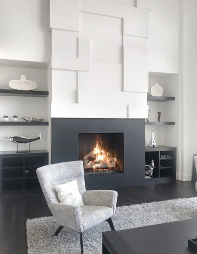 A modern living room with a white armchair in front of a geometric fireplace design.