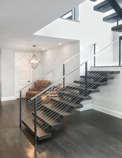 Modern interior with open staircase and cable railing, featuring a geometric light fixture.