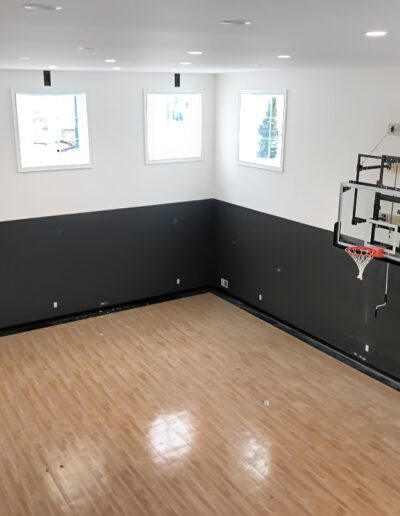 Indoor home basketball court with mounted hoop and hardwood flooring.