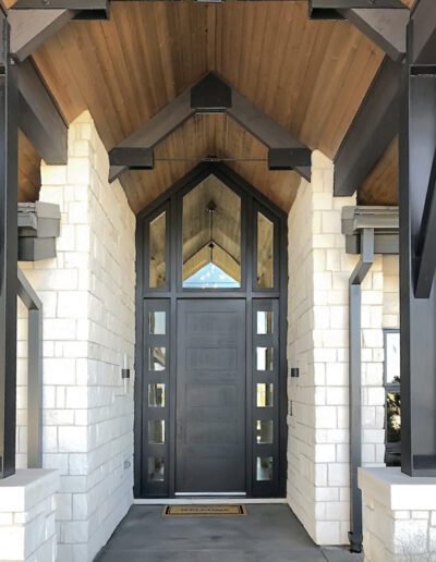 Elegant entryway featuring a tall, dark wood door flanked by stone columns under a wooden gabled porch roof.