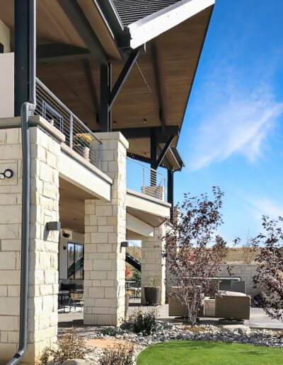 A person standing on the balcony of a modern house with stone pillars and a clear blue sky in the background.