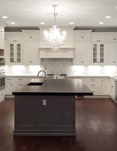Modern kitchen interior with white cabinetry, stainless steel appliances, and a central island under a chandelier.