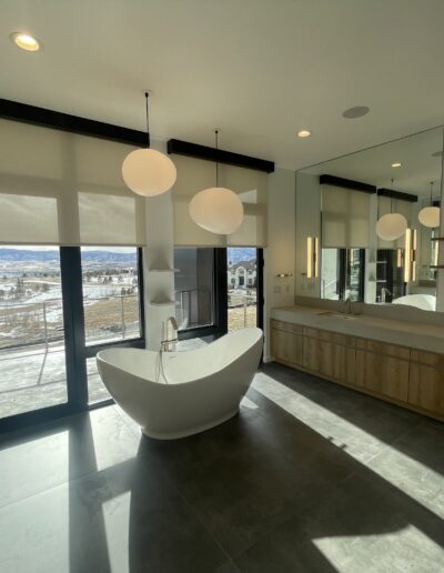 Modern bathroom with a freestanding tub, floating vanity, and spherical pendant lights, featuring large windows with a view of an outdoor landscape.