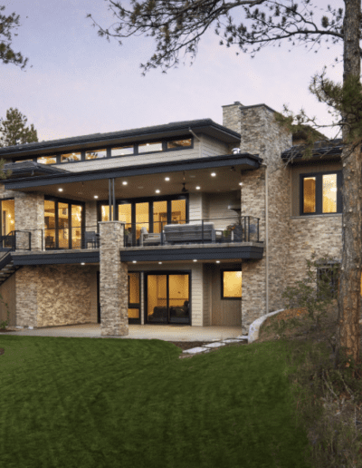 Modern two-story house with stone accents surrounded by pine trees at dusk.