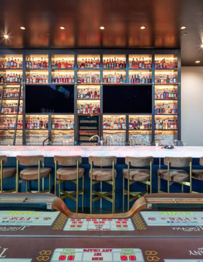 Modern casino interior with a bar featuring a wide selection of beverages and a gaming table in the foreground.