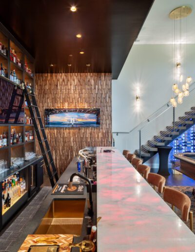 Modern bar interior with an extensive selection of spirits on backlit shelving, a long marble counter, and elegant seating arrangements.