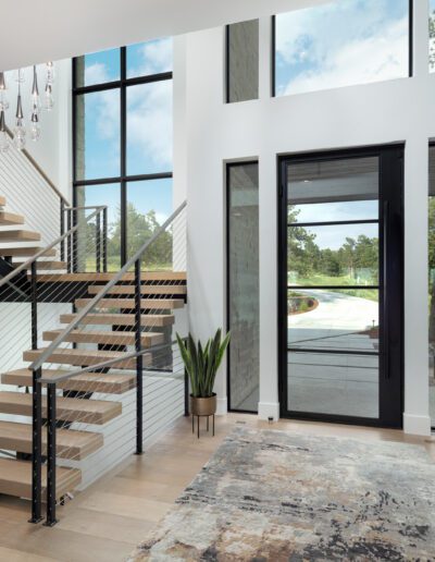 Modern home interior featuring a floating staircase with a black accent wall, large windows, and decorative plants.