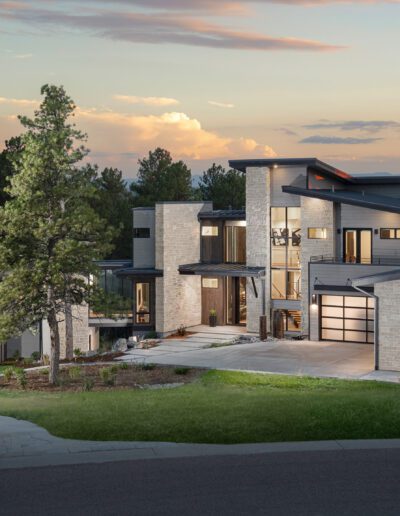 Modern two-story house with a large garage at dusk, surrounded by trees.