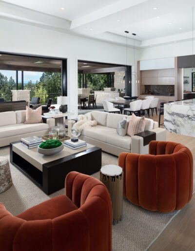 Modern open-plan living room with kitchen, featuring large windows, contemporary furniture, and neutral color palette with orange accents.