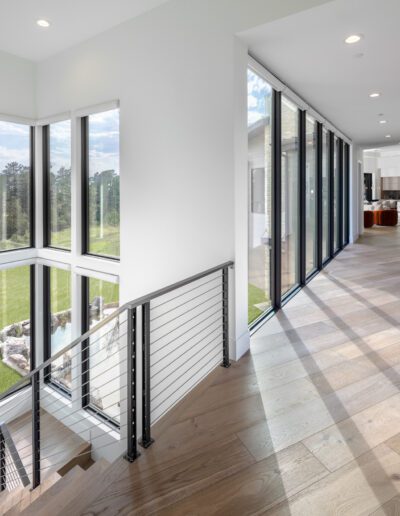 Bright, modern hallway featuring large windows and a wooden floor, leading to an open living area.