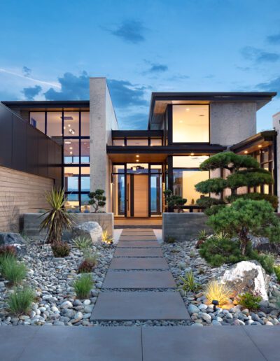 Modern home exterior with glass walls and a landscaped garden at twilight.