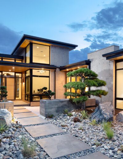 Modern house with large windows illuminated at twilight, featuring a landscaped garden with stepping stones.