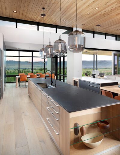 Modern kitchen interior with wood finishes, pendant lights, and a mountain view.