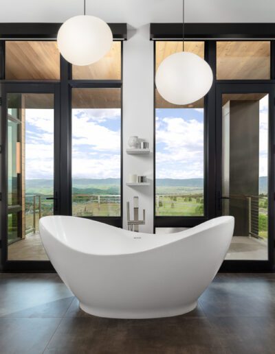 Modern bathroom interior with a freestanding bathtub, dual vanities, and a panoramic view of the landscape through large windows.