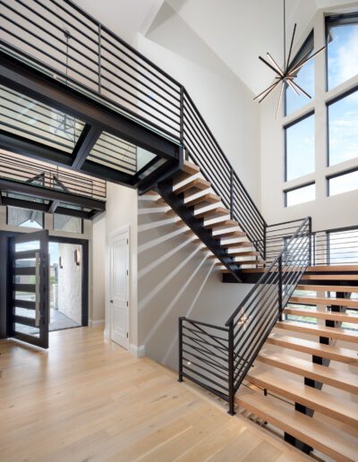 Modern interior with wooden floors featuring a staircase with black metal railings and large windows.